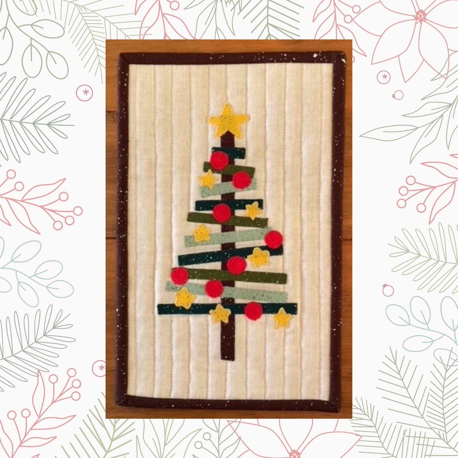 A rectangular quilt with a white background and a brown border. The quilt features a Christmas tree made up of green and brown fabric strips. The tree is decorated with red and yellow ornaments and a gold star. The background is quilted with vertical lines.