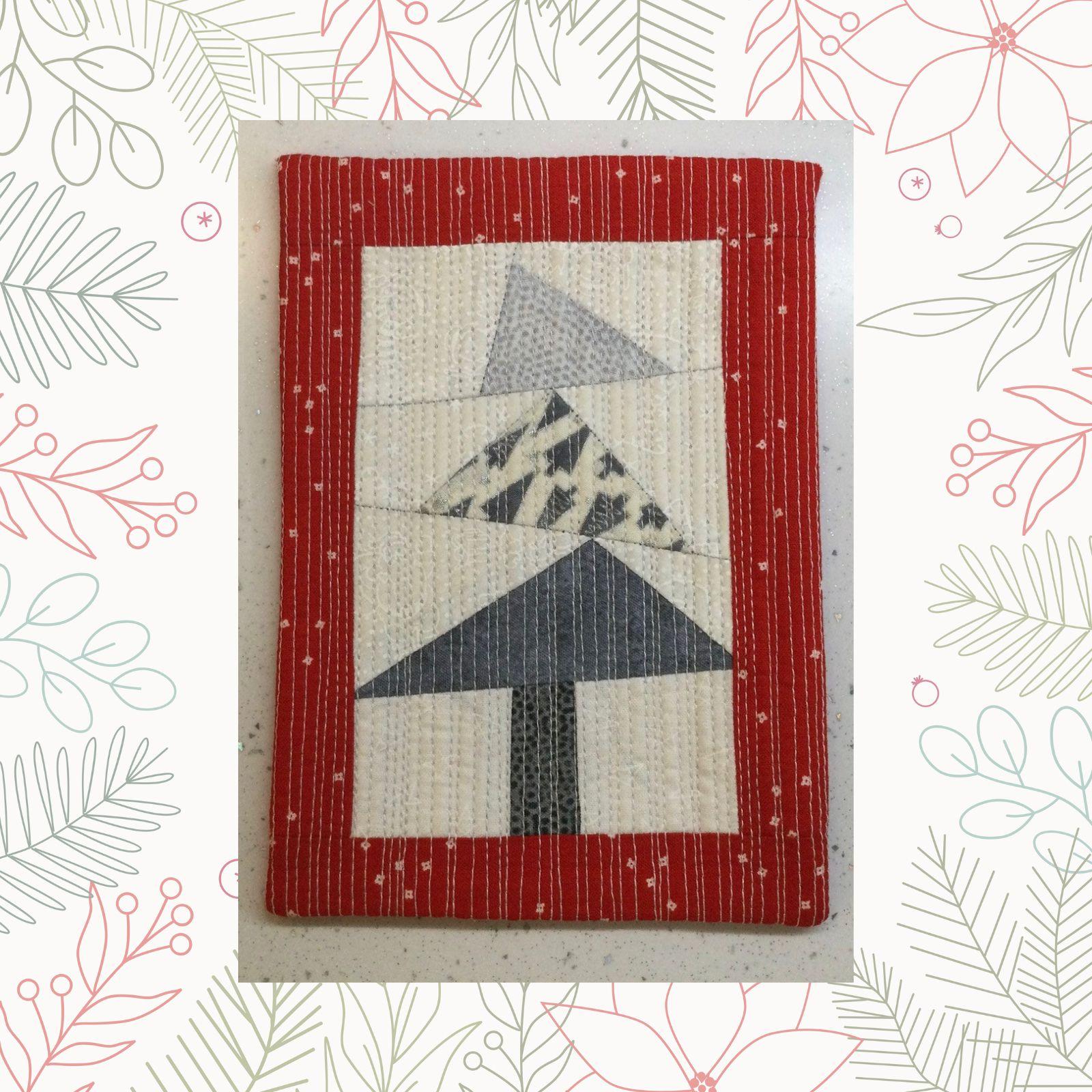 A rectangular quilt with a red background and a white border. The quilt features a Christmas tree made up of triangles in shades of gray and white. The background is quilted with a linear pattern.