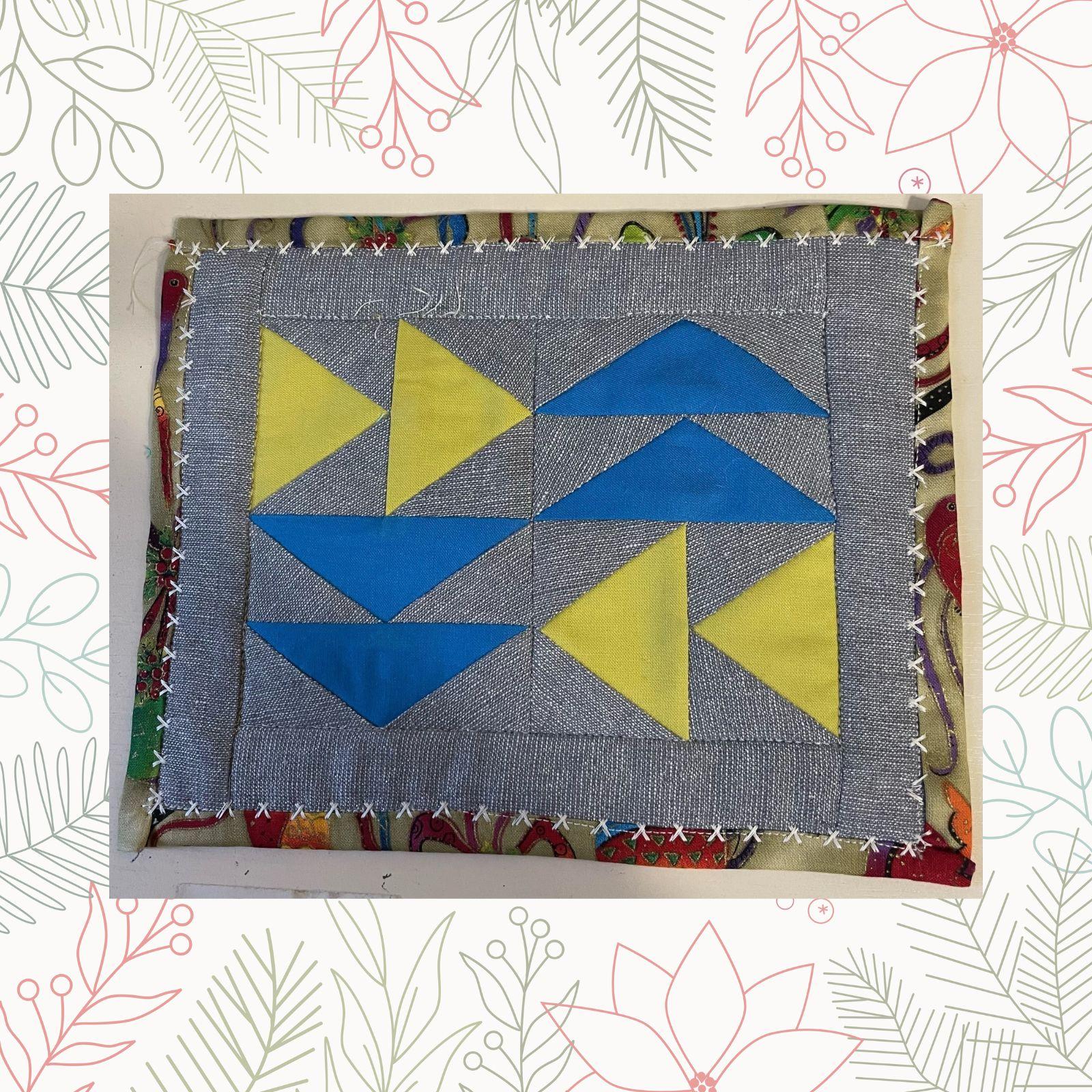 A rectangular quilt with a gray background. The quilt features a pattern of blue and yellow triangles, arranged in a staggered pattern.