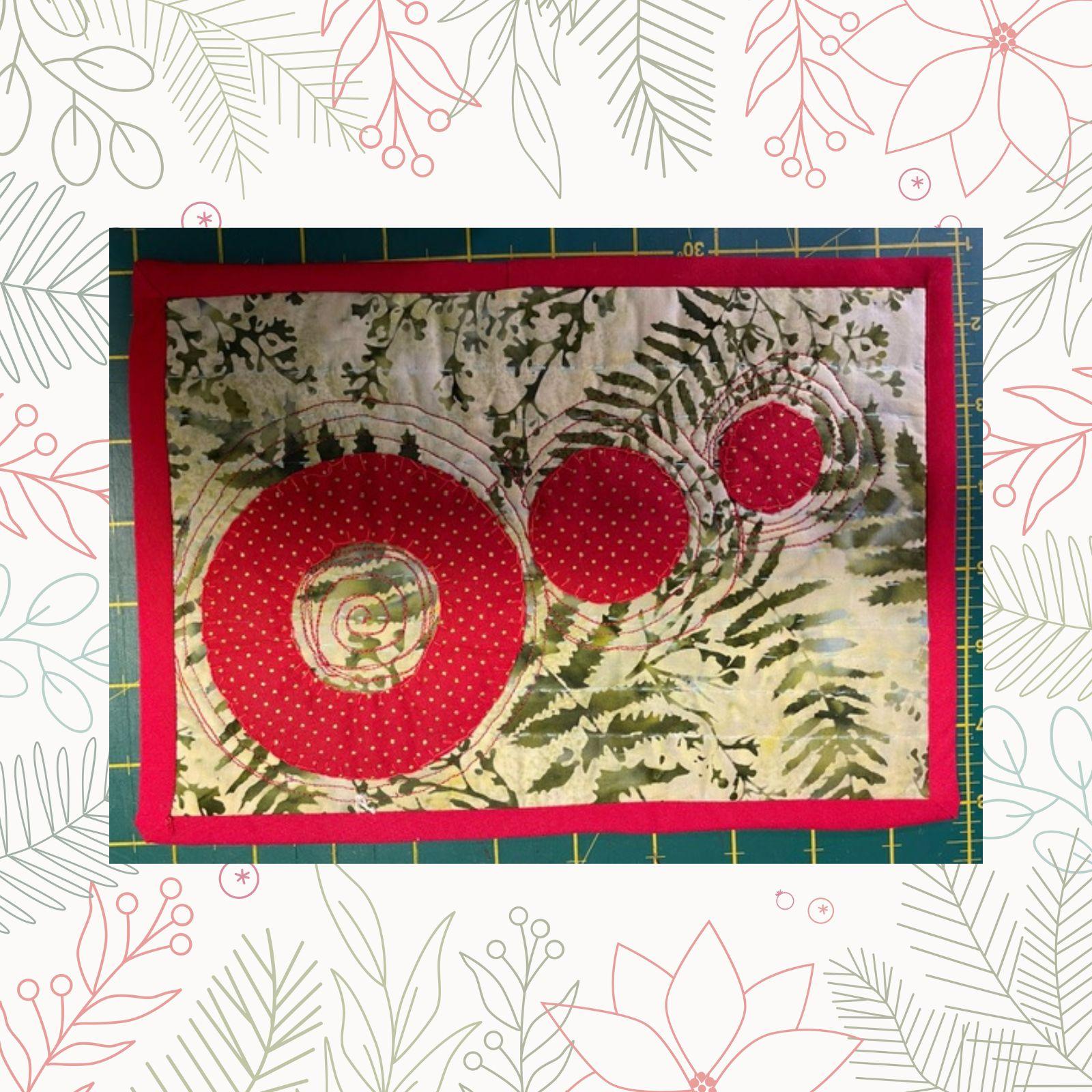 A rectangular quilt with a green background and a red border. The quilt features two large, red circles with smaller circles inside them. The background fabric has a pattern of leaves. The circles are surrounded by a green, leaf-like pattern.