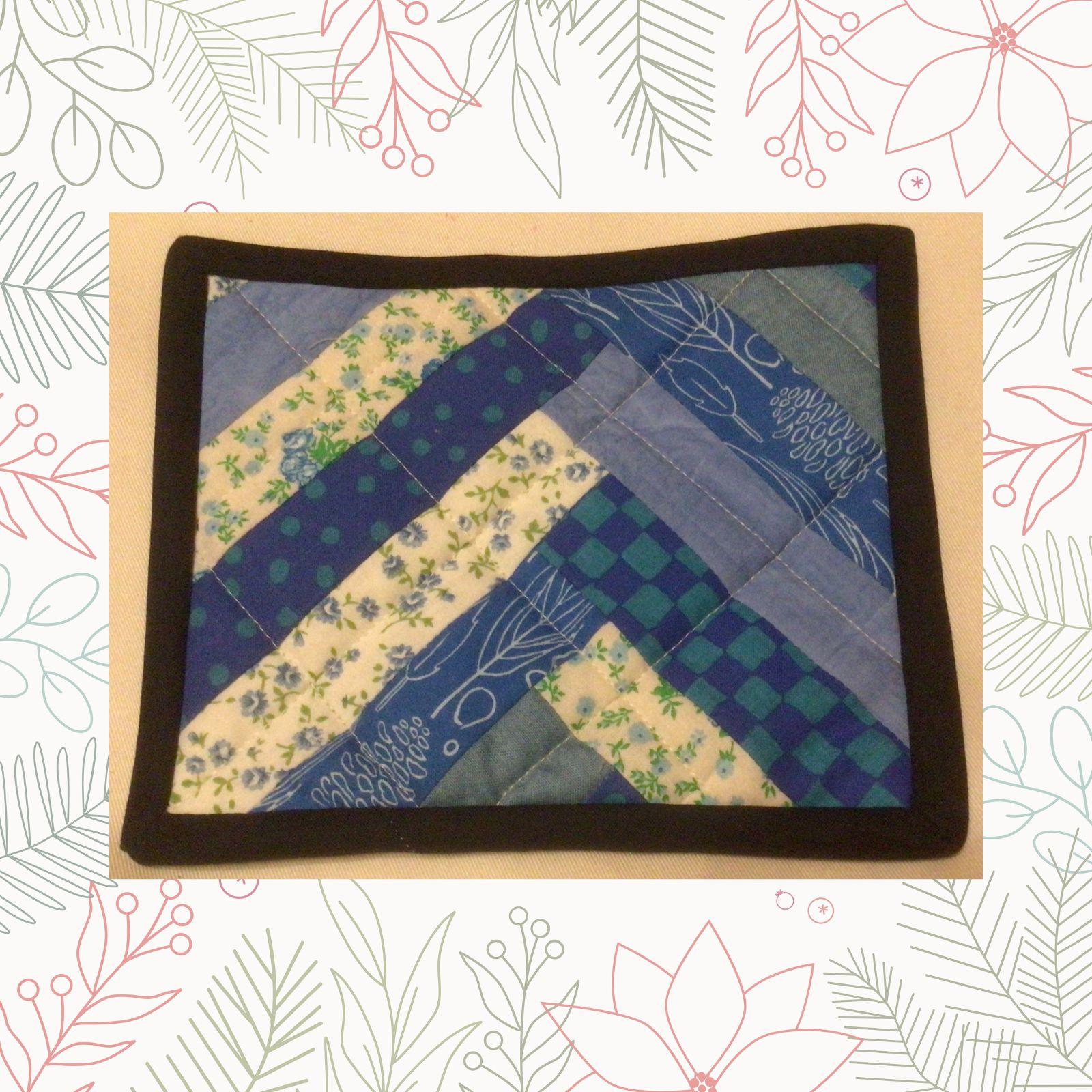 A rectangular quilt with a blue and white patchwork design. The quilt features a chevron pattern made up of various shades of blue and white fabrics. The background is quilted with a linear pattern. The quilt has a black border.