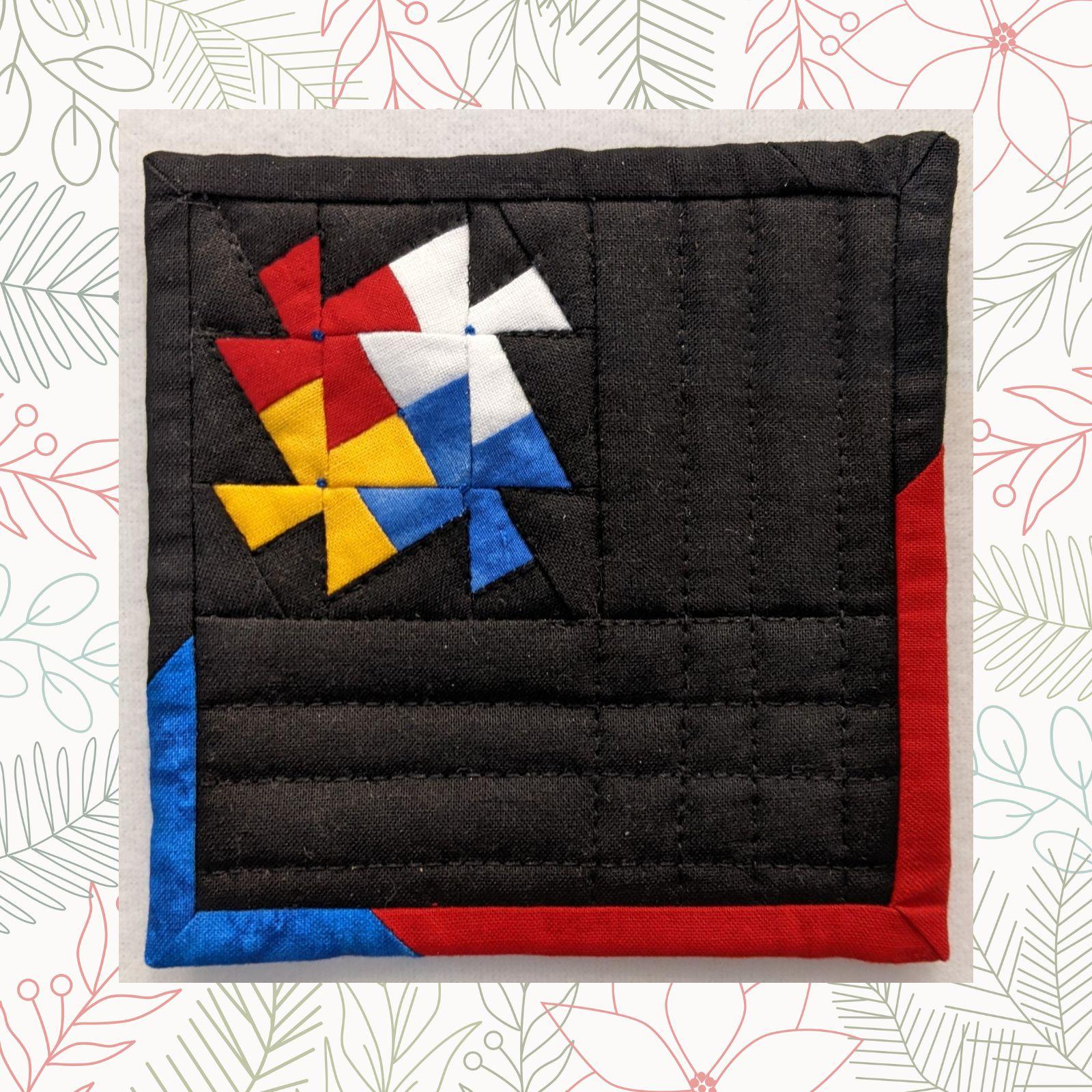 A square quilt with a black background and a colorful, geometric design. The design features a windmill-like shape made up of red, yellow, blue, and white triangles. The background is quilted with a linear pattern. The quilt has a red and blue border.