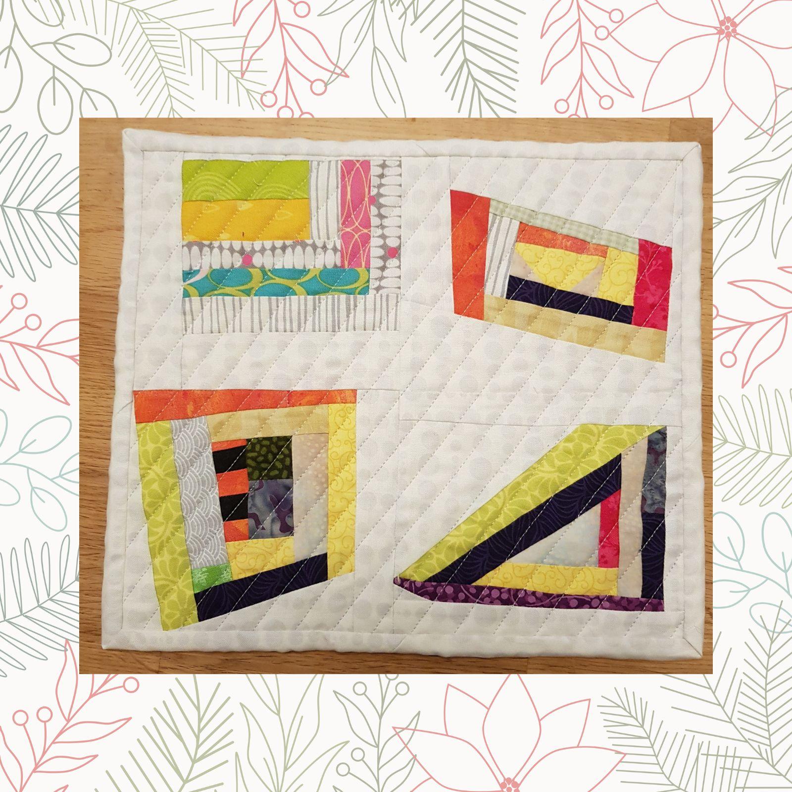 A rectangular quilt with a white background. The quilt features four colorful, geometric designs, each with a different arrangement of squares, rectangles, and triangles. The colors used include yellow, orange, red, green, and blue. The background is quilted with a linear pattern.