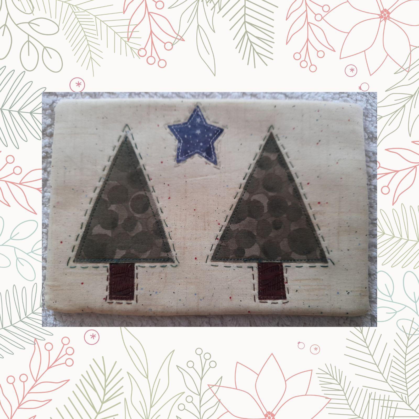 A rectangular quilt with a white background. The quilt features two Christmas trees made from green fabric with a speckled pattern. A blue star is placed between the trees.