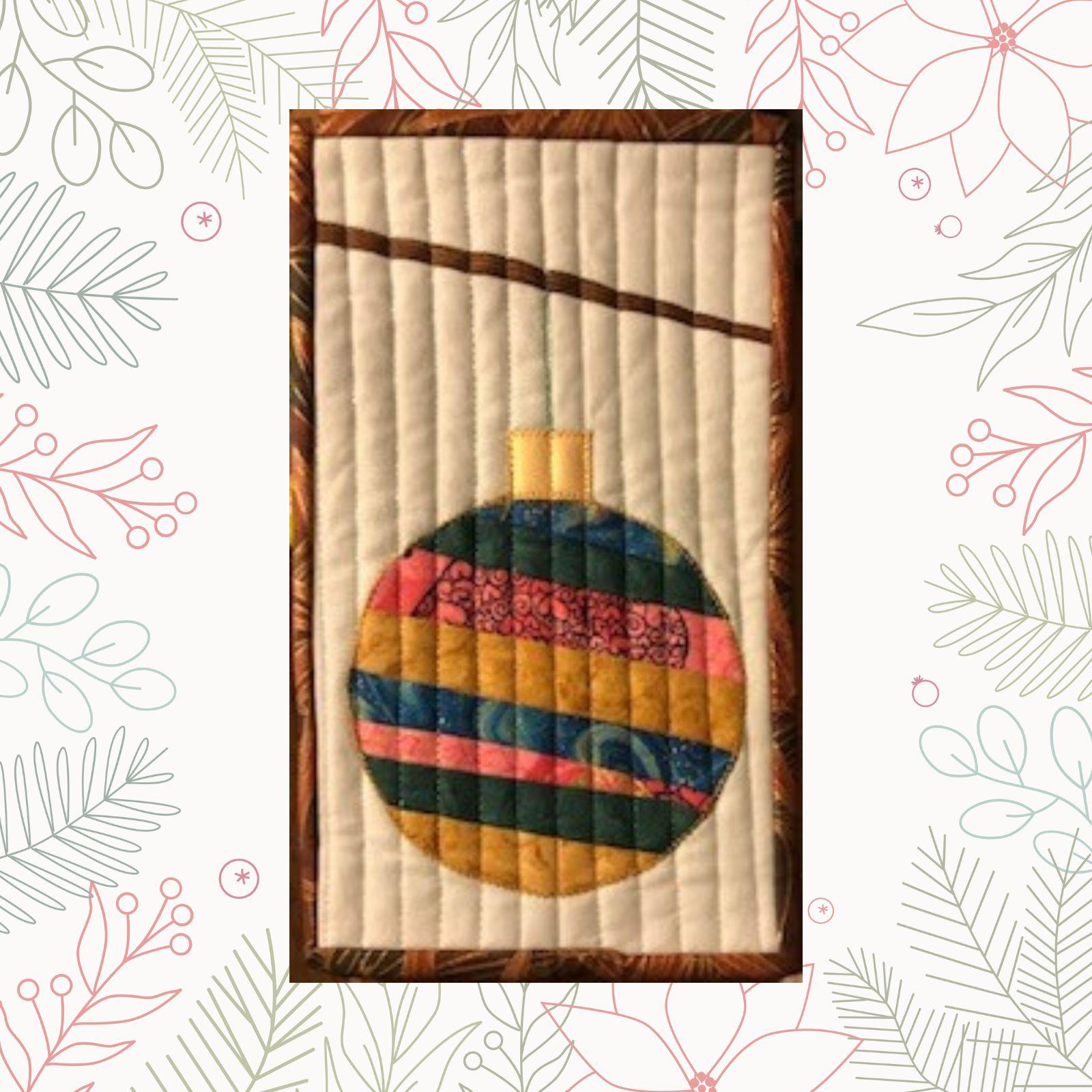 A rectangular quilt with a white background and a brown border. The quilt features a colorful Christmas ornament hanging from a string. The ornament is made up of strips of fabric in various colors, including pink, blue, and green. The background is quilted with vertical lines