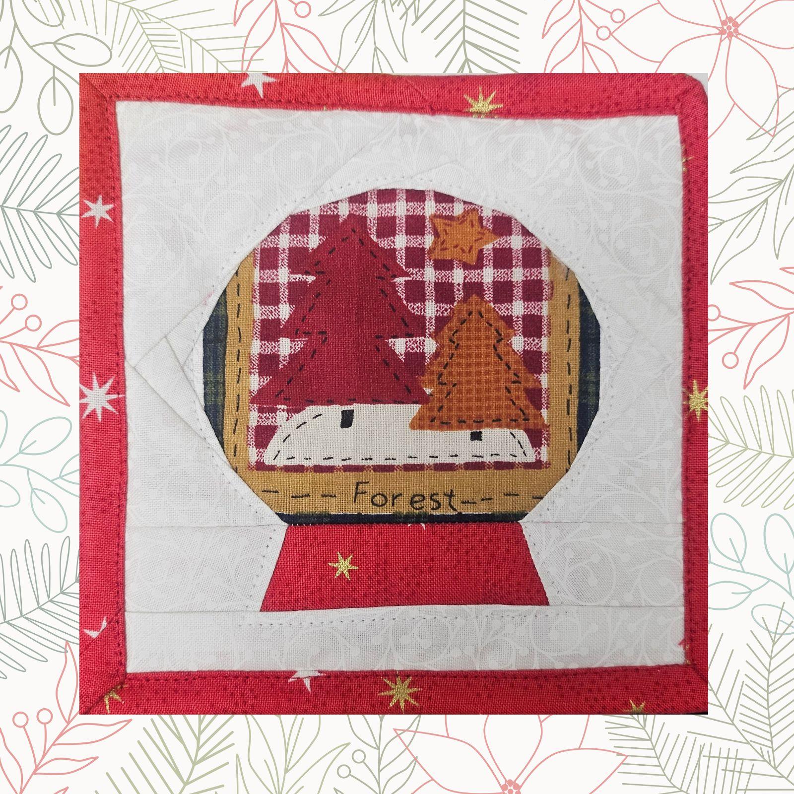 A square quilt with a red background. The quilt features a circular window with a winter scene inside, showing trees and snow. The words "Forest" are embroidered at the bottom of the window.