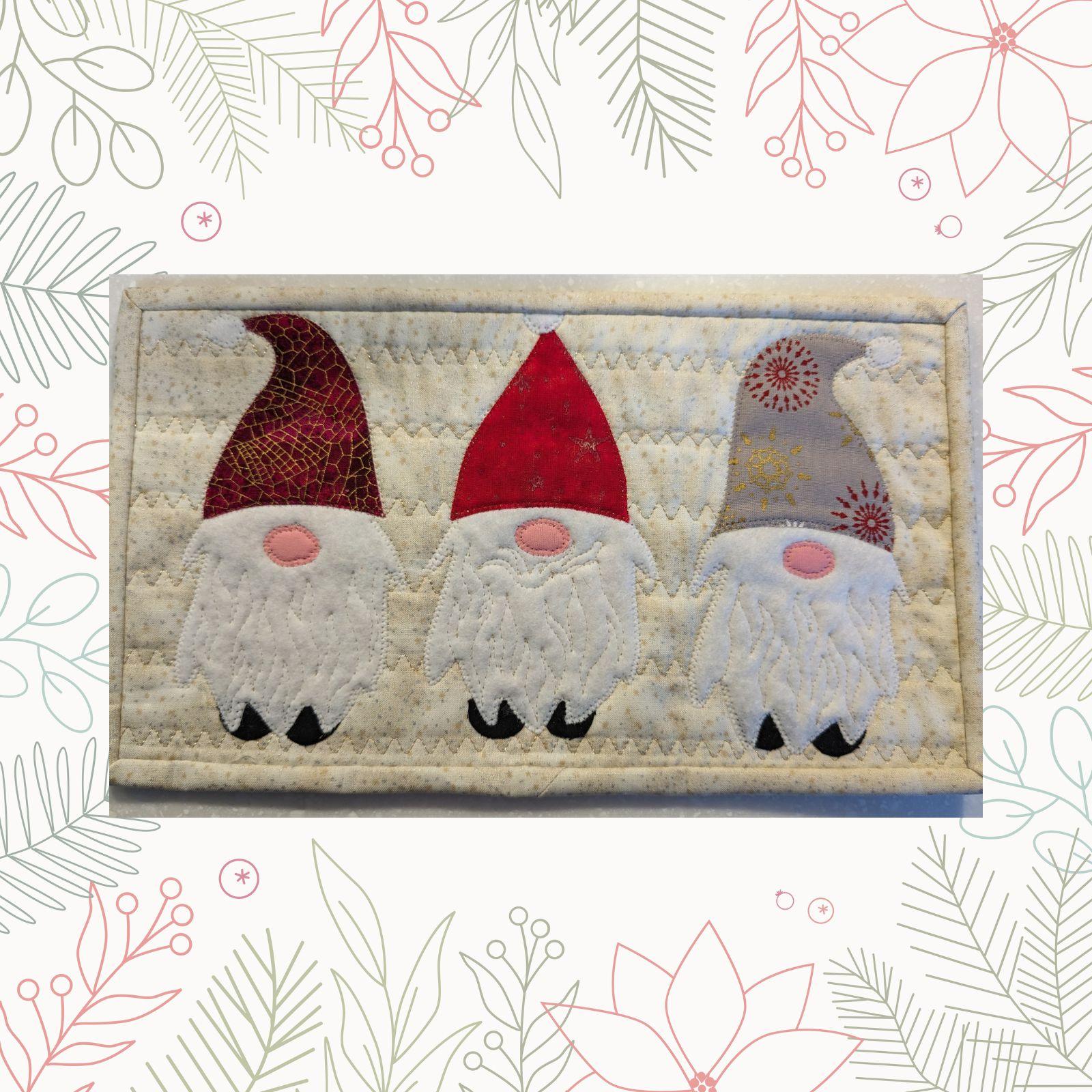 A rectangular quilt with a white background. The quilt features three gnomes standing side by side. Each gnome has a different colored hat and beard, and their bodies are made of different fabrics. The background is quilted with a short wavy line.