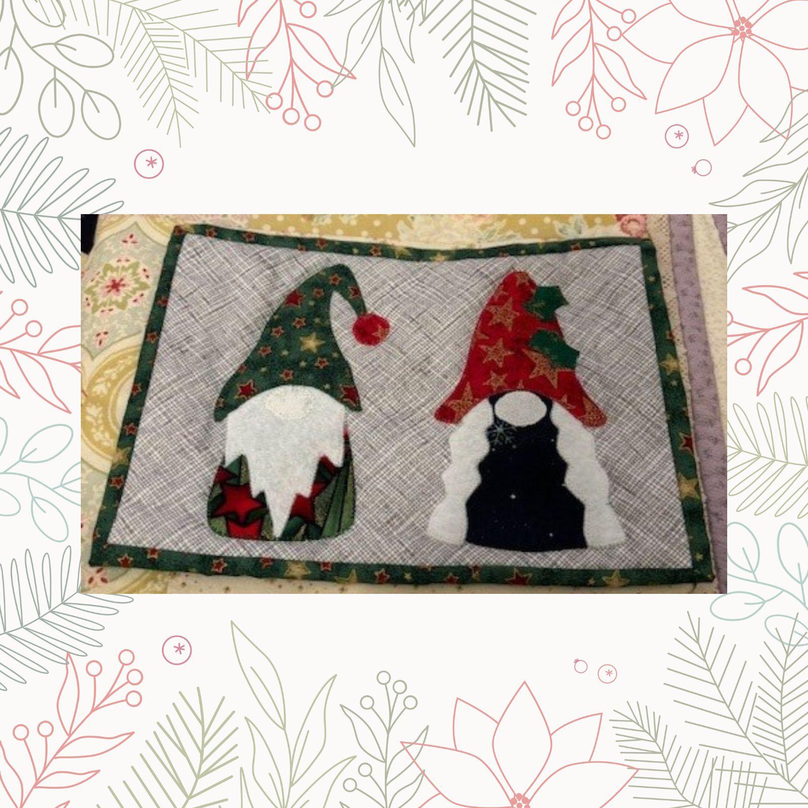 A rectangular quilt with a gray background and a green border. The quilt features two gnomes with colorful hats and beards. The gnomes are made of fabric with different patterns and textures.