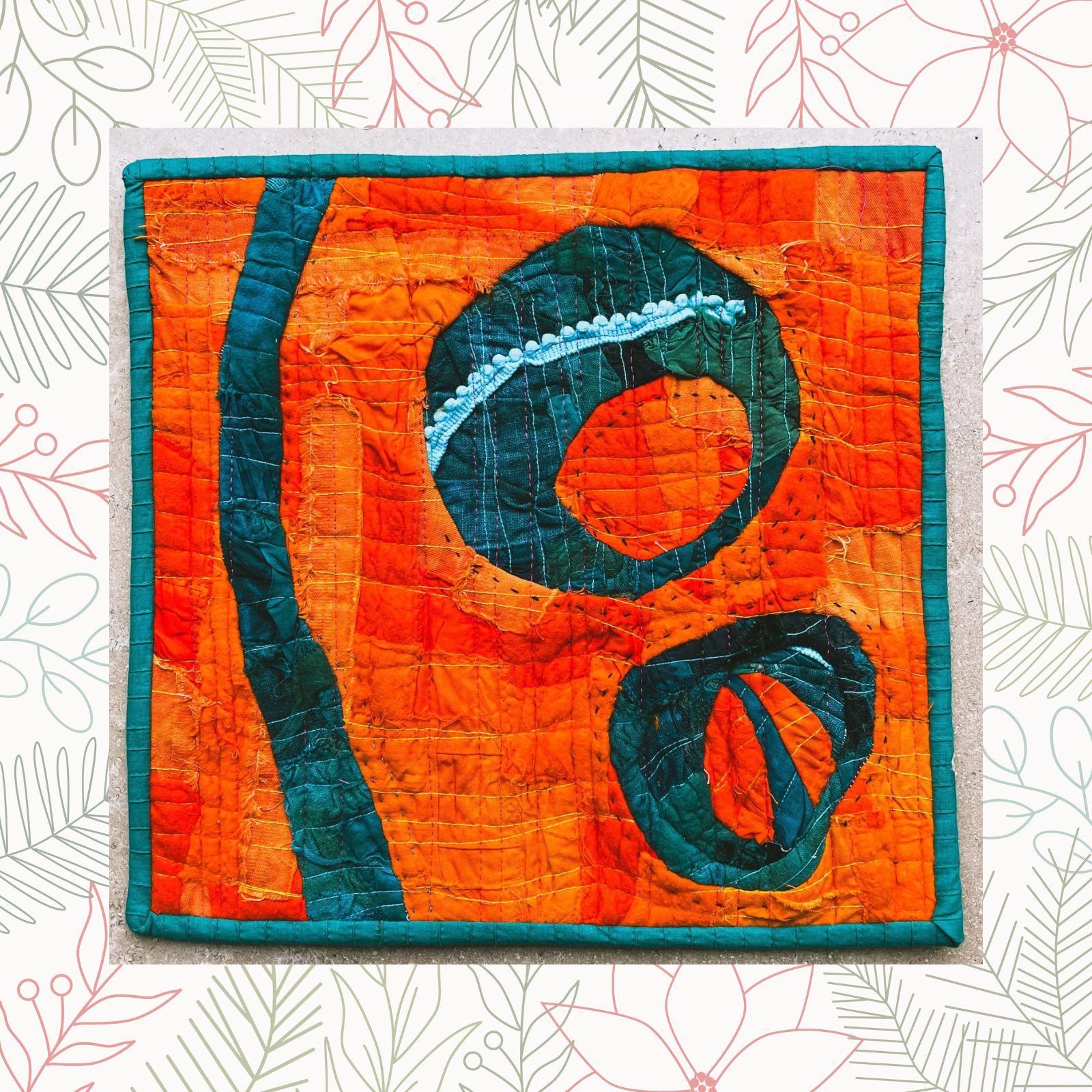 A square quilt with an orange background and a green border. The quilt features two large, green, organic shapes, one with a scalloped edge. There is a thin, blue, wavy line running through the orange background. The background is quilted with a linear pattern.