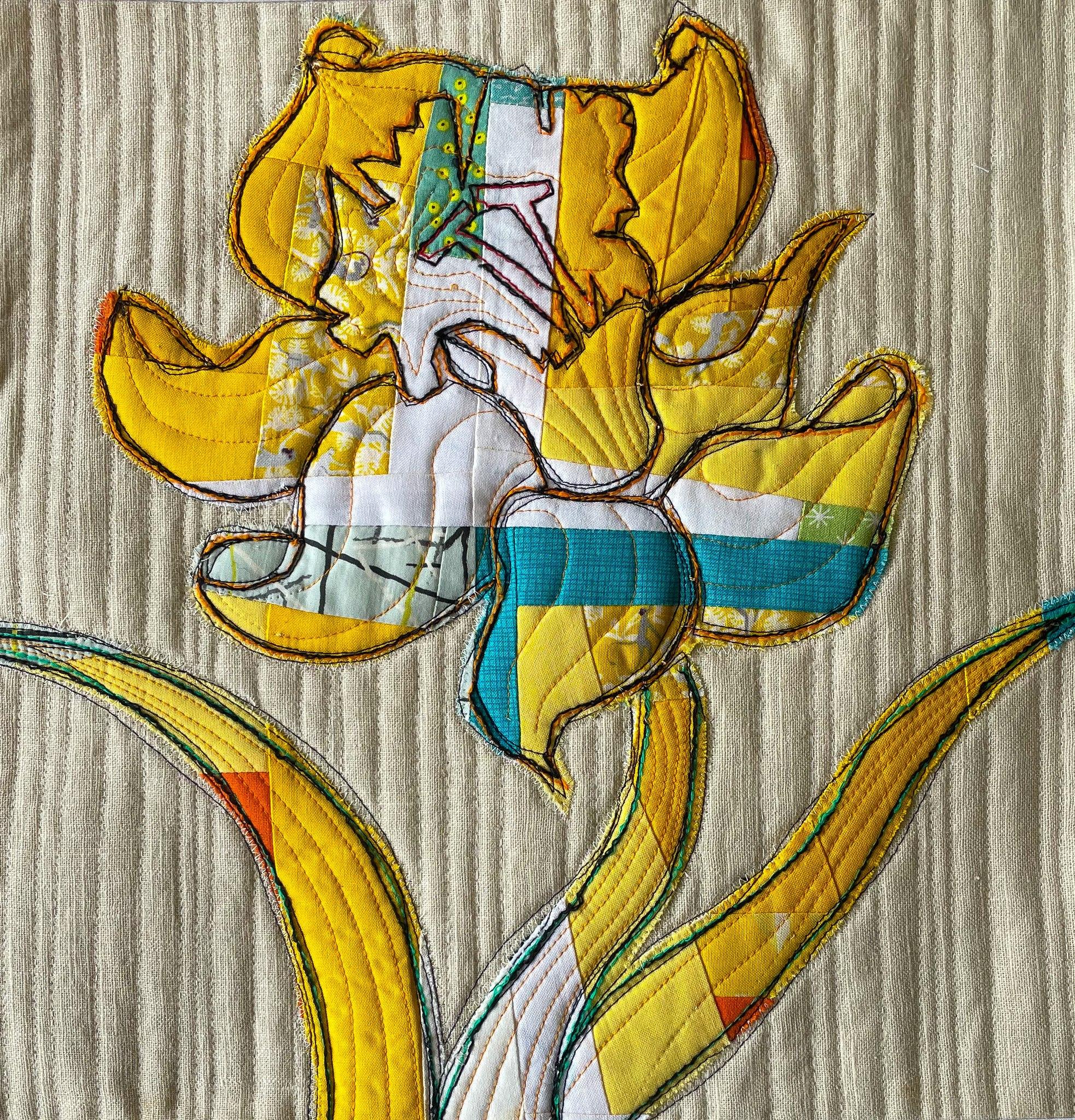 A close-up of a yellow, quilted placemat with a flower as the central motif. The flower is made up of various shades of yellow fabric and has a detailed, quilted texture. The background is a textured, off-white fabric.