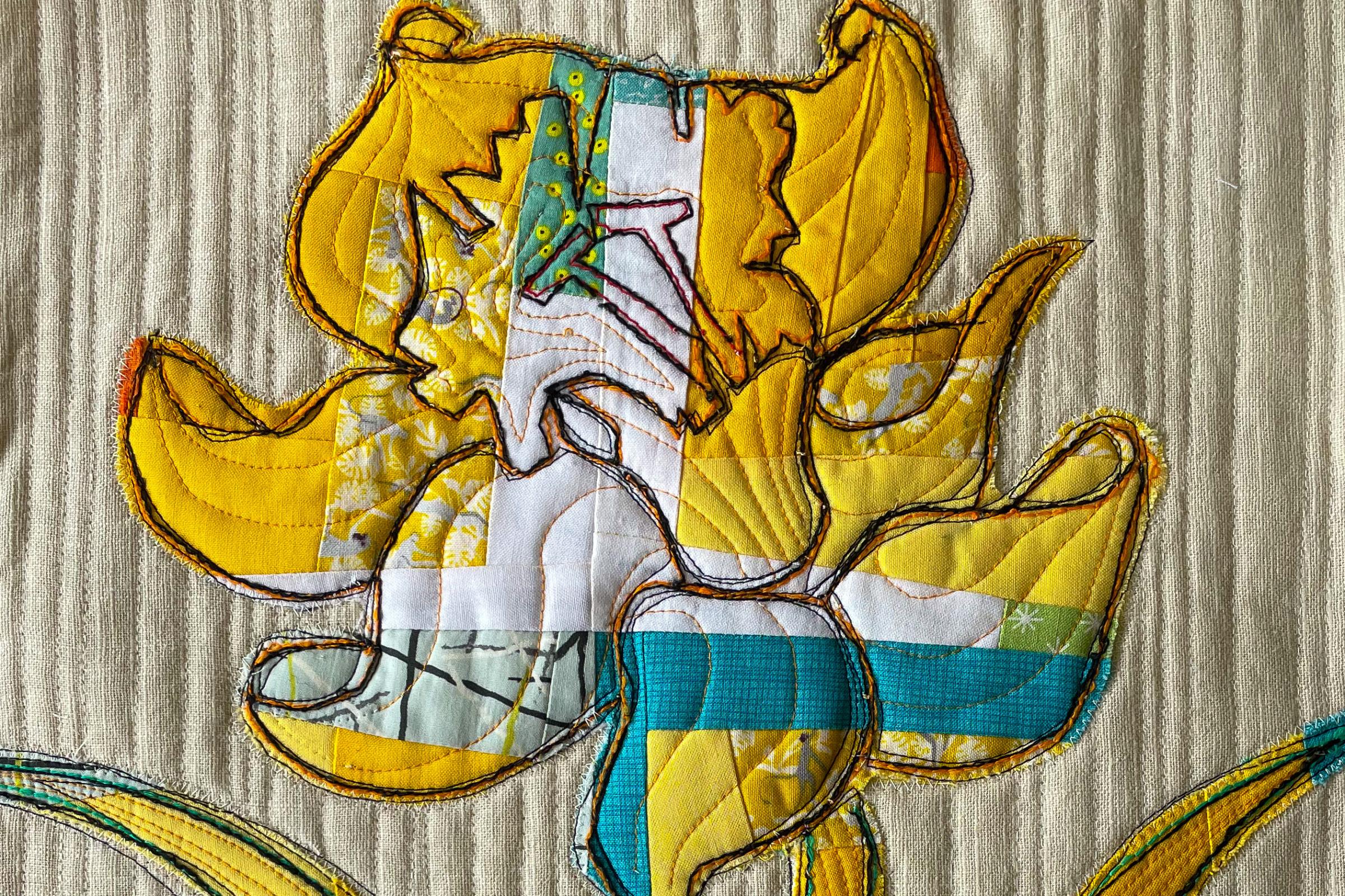 A close-up of a yellow, quilted placemat with a flower as the central motif. The flower is made up of various shades of yellow fabric and has a detailed, quilted texture. The background is a textured, off-white fabric.