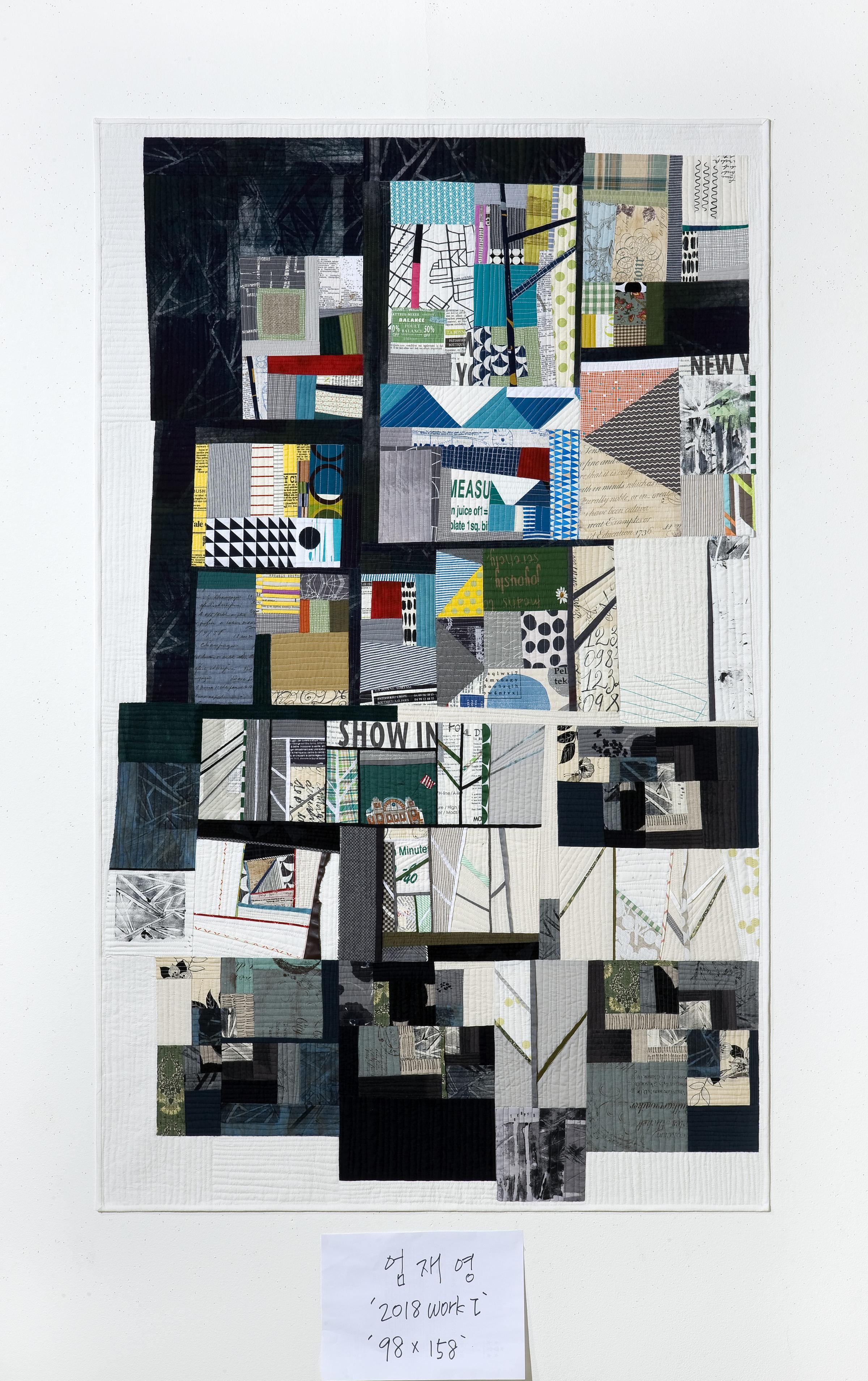 A large, abstract quilt with a predominantly black background. The quilt is composed of various shapes and patterns in black, white, gray, and pops of color like red, yellow, and green. There are geometric shapes, organic forms, and textural elements, creating a complex and visually interesting composition. The quilt appears to be made up of numerous smaller pieces of fabric sewn together.