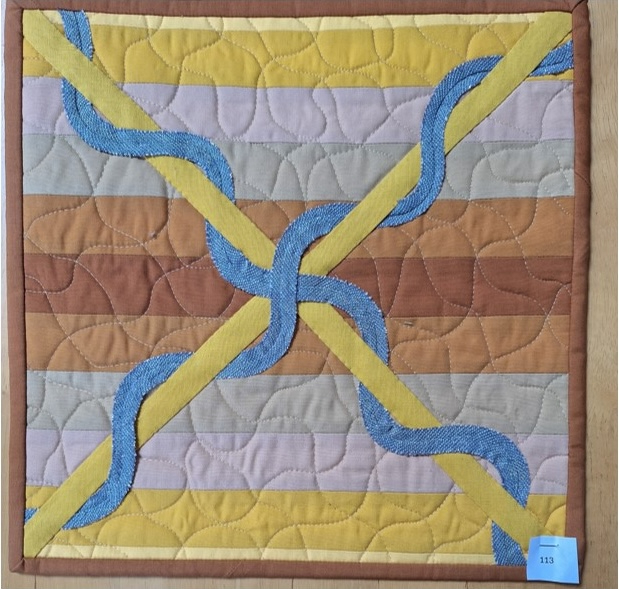 A square quilt with a brown background and a brown border. The quilt features two intersecting, wavy lines in blue and yellow. The background is quilted with a wavy line hatched pattern.