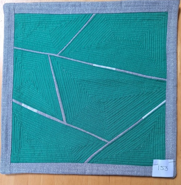 A square quilt with a green background and a gray border. The quilt features a geometric design with intersecting lines creating shapes like triangles and rectangles. The lines are white and the background is quilted with a linear pattern.