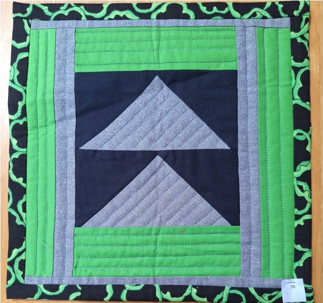 A square quilt with a green background and a green border. The quilt features two gray triangles pointing upwards, set against a black square. The background is quilted with a linear pattern.