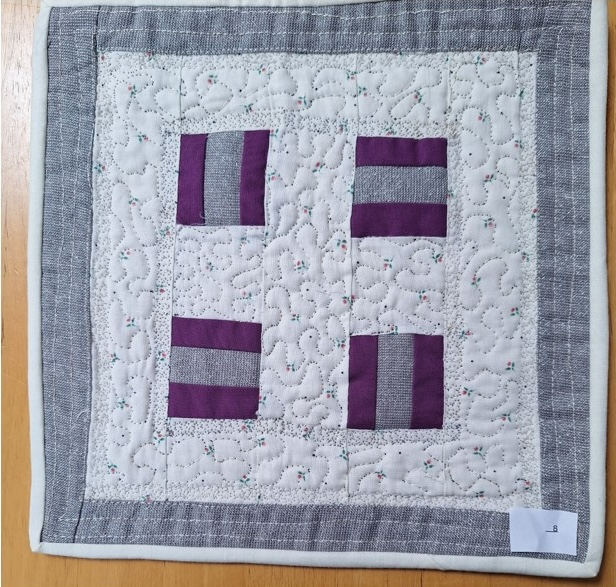 A square quilt with a white background and a gray border. The quilt features four purple rectangles arranged in a cross shape. The background is quilted with a stipple pattern.
