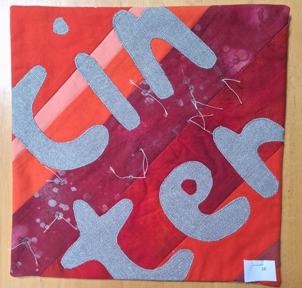 A square quilt with a red background and a red border. The word "TINTER" is spelled out in gray letters on a diagonal red striped background.