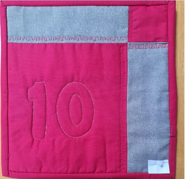 A square quilt with a red background and a gray border. The quilt features the number "10" in white stitching