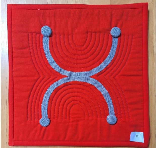 A square quilt with a red background and a gray border. The quilt features a gray, curved "X" shape with four circular buttons at the ends of the lines. The background is quilted echoing the quilt feature