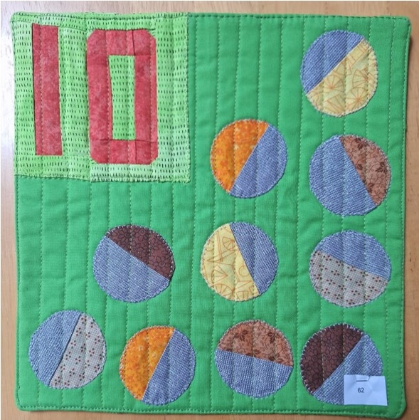 A square quilt with a green background and a green border. The quilt features the number "10" in red in the top left corner and several colourful circles with different patterns and textures. The background is quilted with vertical lines.