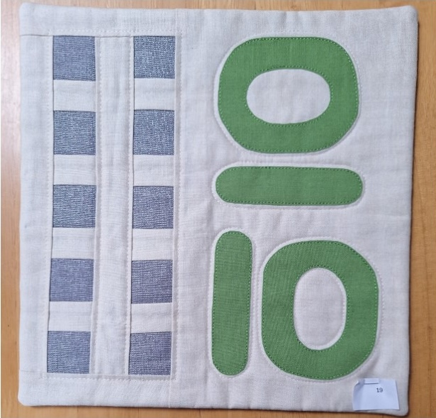 A square quilt with a white background and a gray border. The quilt features the number "10" in green
