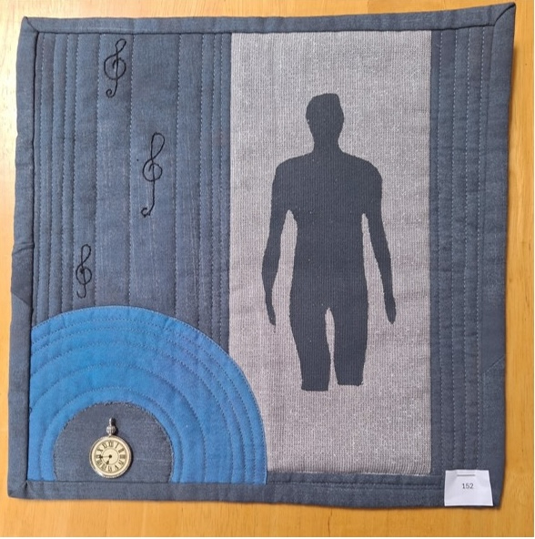 A square quilt with a blue background and a gray border. The quilt features a gray human figure on the right side and a blue circle with musical notes on the left side. A small pocket watch is attached to the circle. The background is quilted with a linear pattern.
