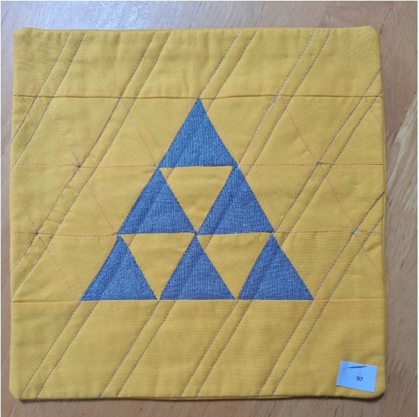 A square quilt with a yellow background and a yellow border. The quilt features a large, gray triangle made up of smaller, overlapping triangles. The background is quilted with a diagonal line pattern.