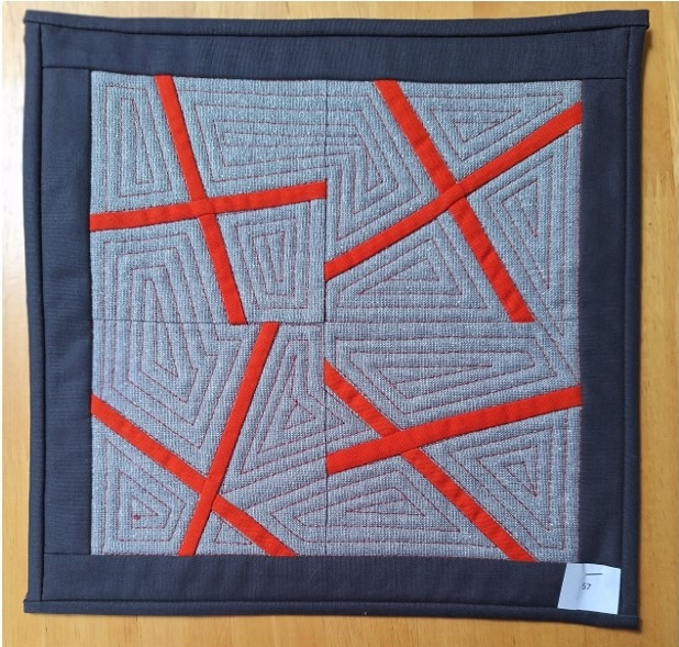 A square quilt with a gray background and a gray border. The quilt features a geometric design with intersecting red lines creating a pattern of squares and triangles. The background is quilted with an irregular shape pattern in between the crosses.