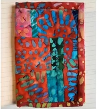 A red quilted needle case with a patchwork design. The patchwork features various shades of red, blue, and green batik fabric with a swirling pattern.