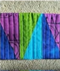 A quilted needle case with a patchwork design in shades of purple, green, and blue. The case features a triangular pattern and has a quilted texture.