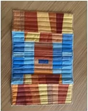 A colorful quilted needle case with a patchwork design. The patchwork features vertical stripes in shades of brown, yellow, blue, and red.