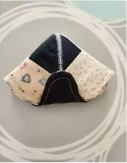 A black and cream quilted needle case with a patchwork design. The case is shaped like a triangle and has a scalloped edge.