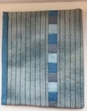 A blue quilted needle case with a vertical stripe of blue squares on the right side. The background fabric has a subtle striped pattern.