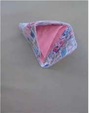 A triangular quilted needle case with a pink interior and a blue and white floral exterior. The case is folded in half, showing both the inside and outside.