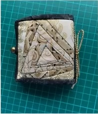 A beige and brown quilted needle case with a triangular patchwork design. The case has a small metal clasp and a string tie.