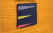 A blue quilted needle case with a patchwork design. The patchwork features triangles in shades of purple, yellow, and pink.