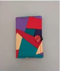 A colorful quilted needle case with a patchwork design. The patchwork features various shapes and colors, including red, purple, teal, and yellow. A red button is visible on the front of the case.