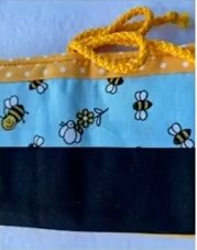 A blue and yellow quilted needle case with a bee theme. The case has a black bottom section and a blue top section with a pattern of bees and flowers. It closes with a yellow drawstring.