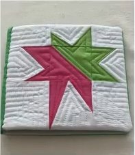 A green quilted needle case with a pink and green star design on the front. The star is made up of triangles and has a quilted texture.
