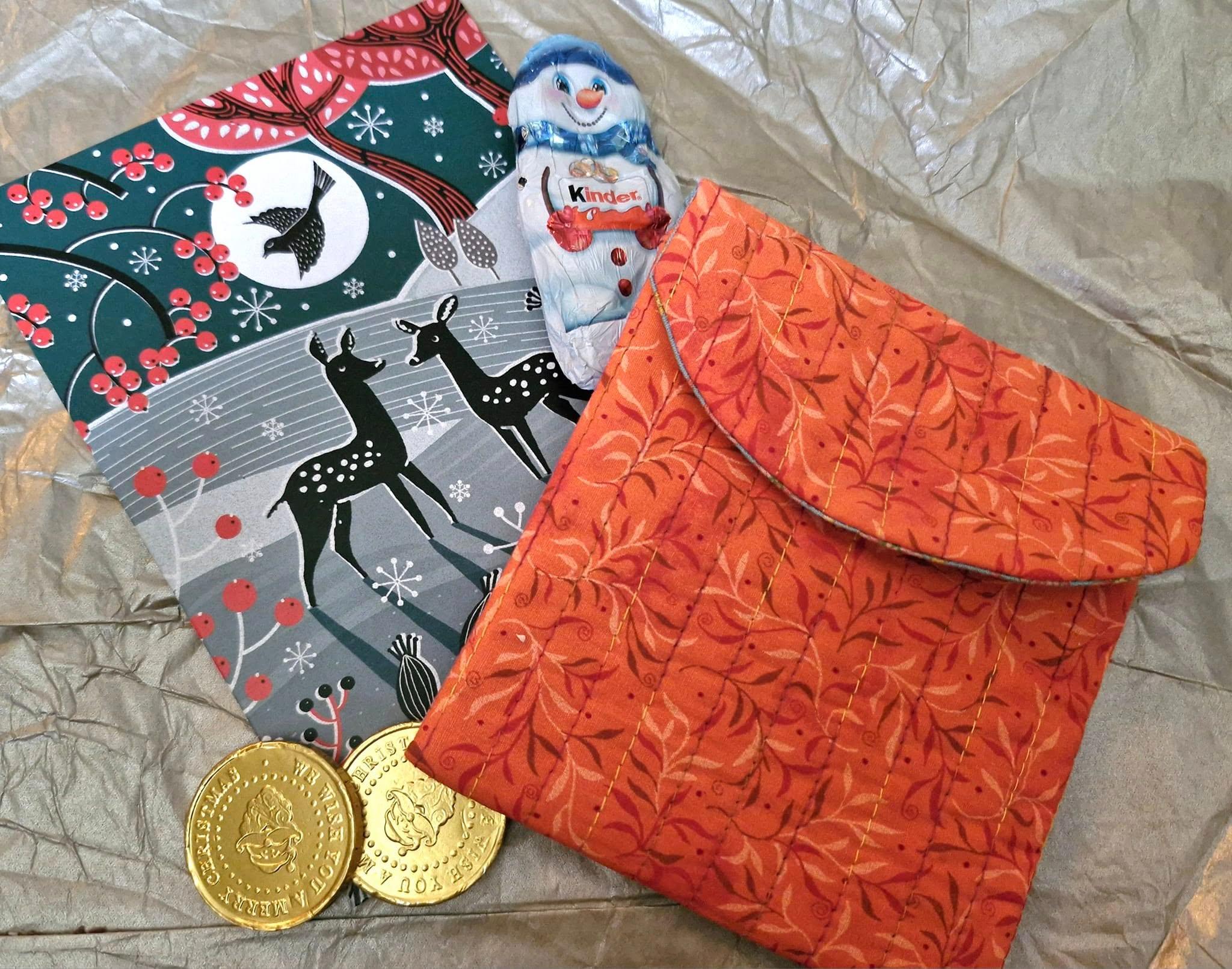 A small, handmade orange floral patterned pouch. It has a flap with a straight line quilting.