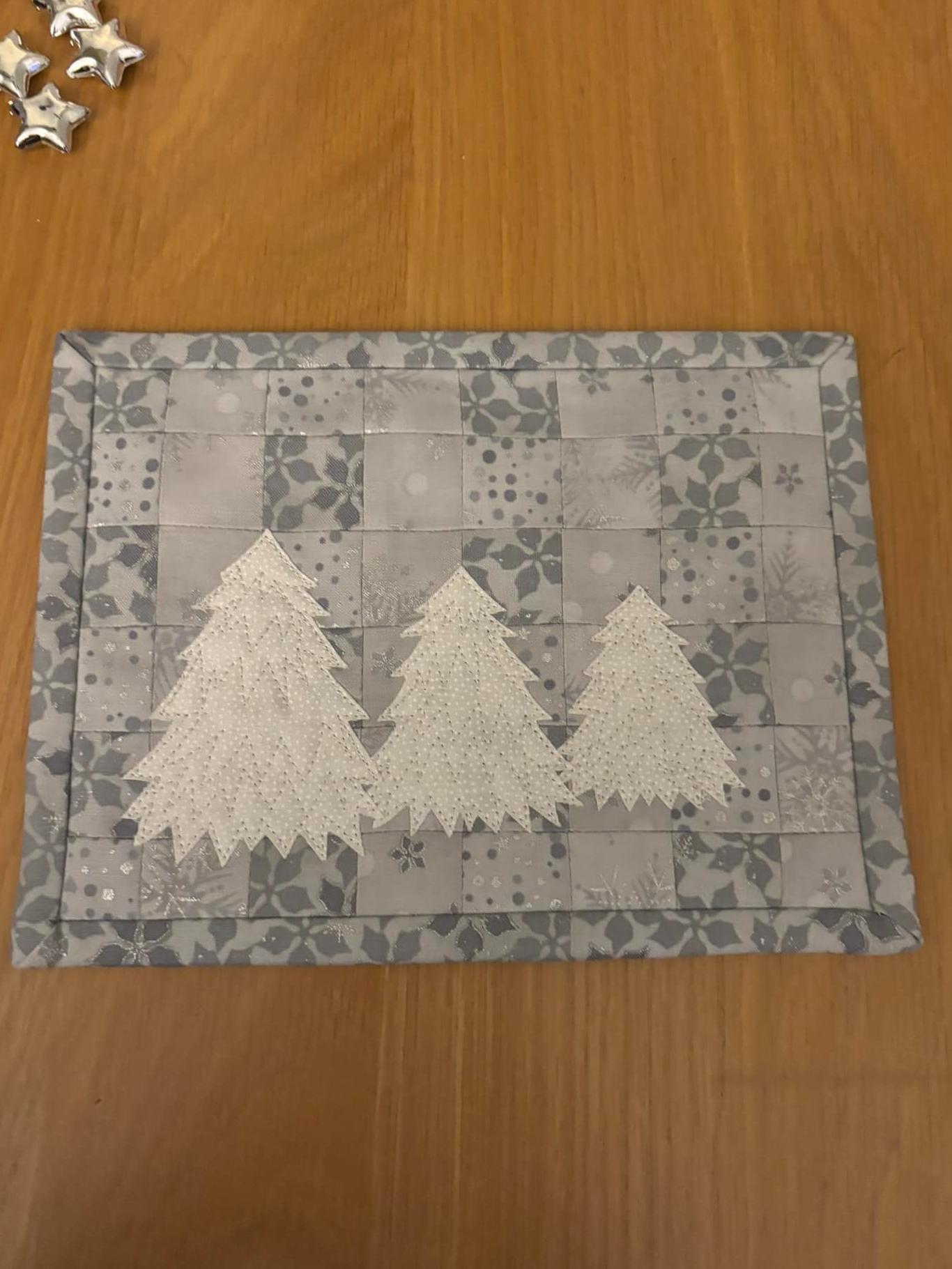 Patchwork mini quilt in silver fabrics with three white trees in the foreground.