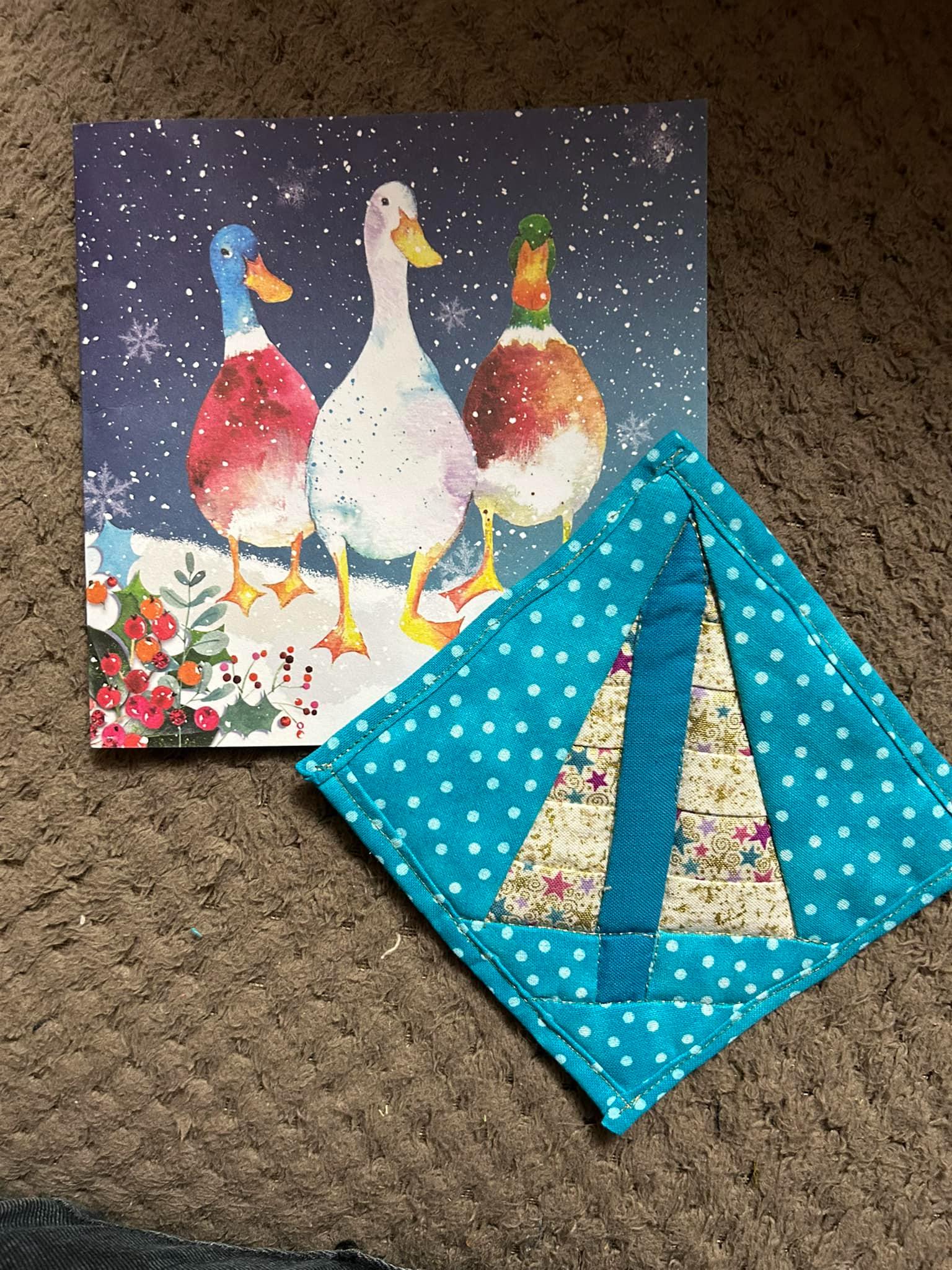 A blue spotty coaster with a pieced Christmas tree in the centre. Off to the top left of the photo is a Christmas card with ducks.