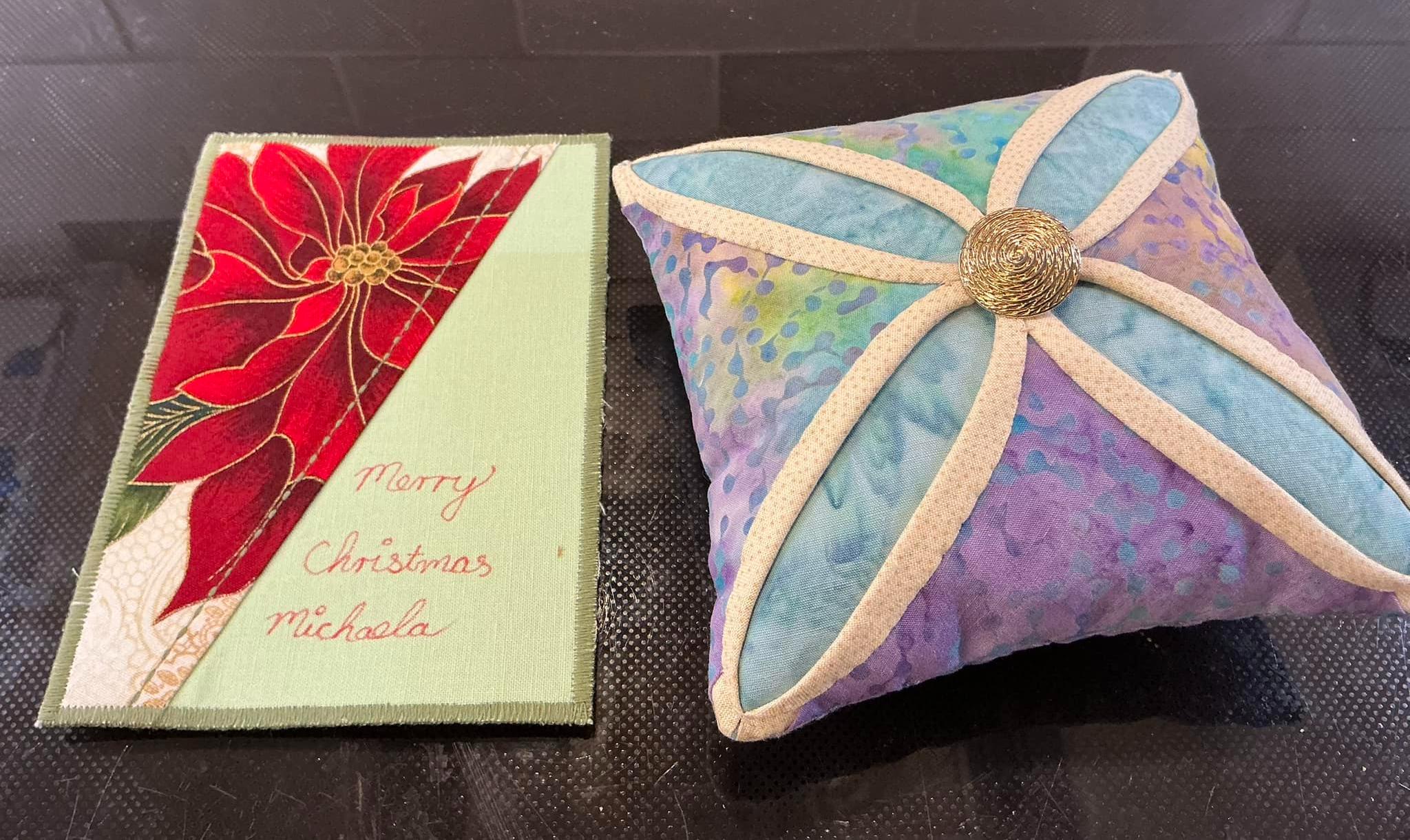 A beautiful pin cushion made from purple and blue batik fabrics. At the centre is a gold button.