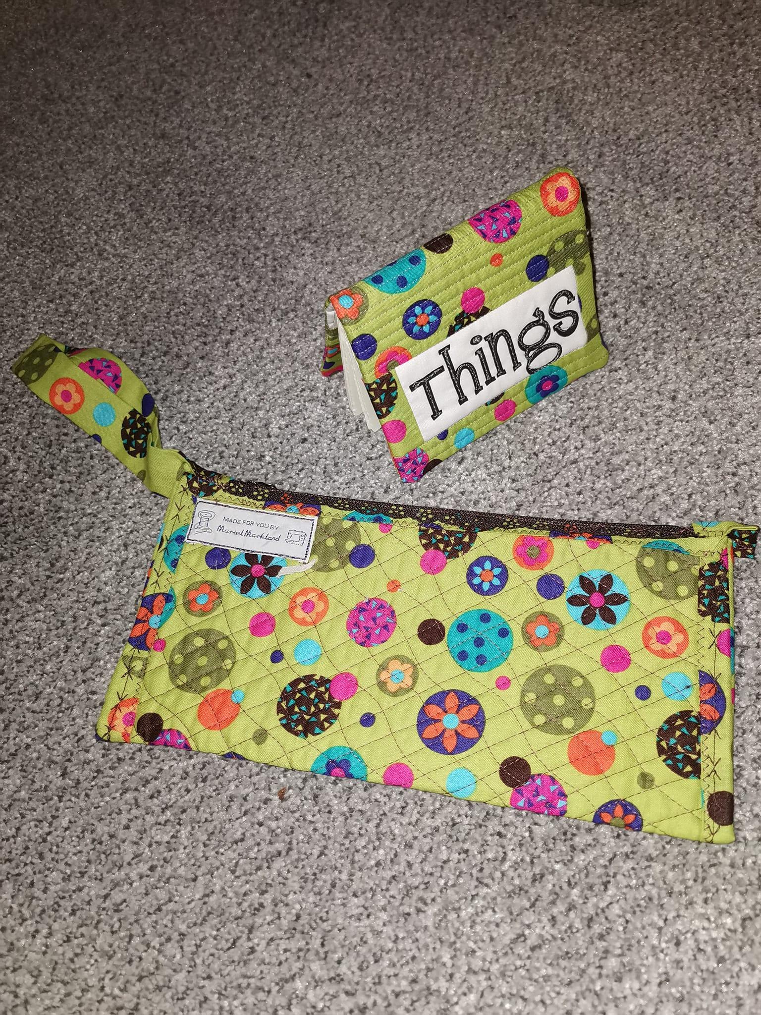 A notebook cover made of a lime green fabric decorated with various patterned circles similar to Christmas baubles. In the foreground is a pouch made of the same material that features a tag in the top left corner.