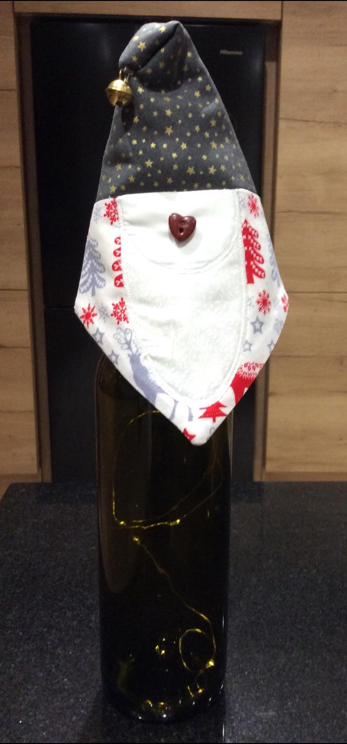 A Santa head bottle topper on a bottle of wine. Santa has a button nose and a small bell atop his hat.
