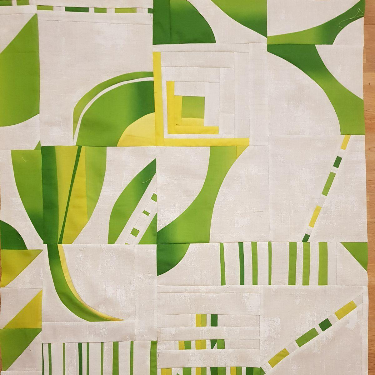 Pieced quilt top in shades of green and yellow on a white background, featuring abstract geometric shapes and lines.