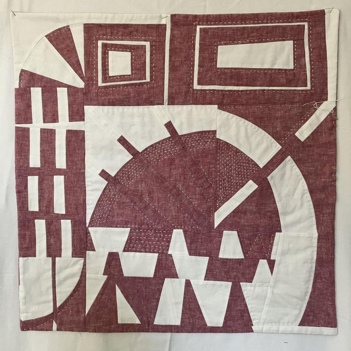 Abstract quilt top in burgundy and white, featuring geometric shapes and lines.