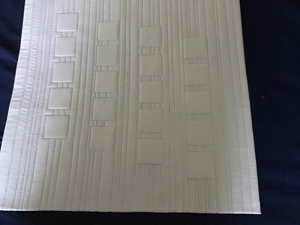 A quilt with a white background. The quilt features five vertical lines of squares, with each square outlined by a quilted line. The background is quilted with horizontal lines.