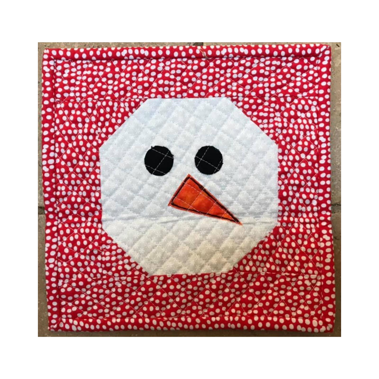  A square quilt with a red background and white polka dots. A white circle with a black button nose and eyes is centred on the quilt, representing a snowman's face.