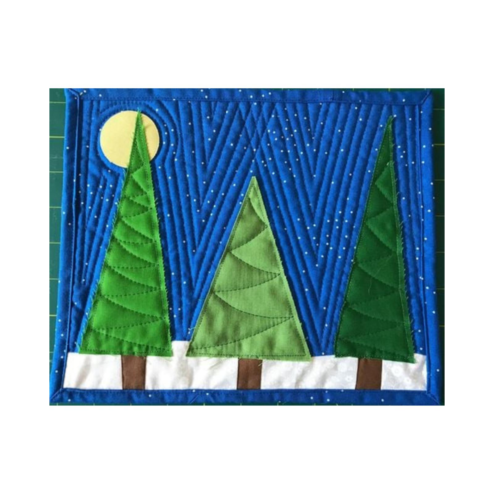 A rectangular quilt with a blue background. The quilt features three green Christmas trees on a white, snowy ground. There is a yellow moon in the top left corner. The background is quilted with a linear pattern.